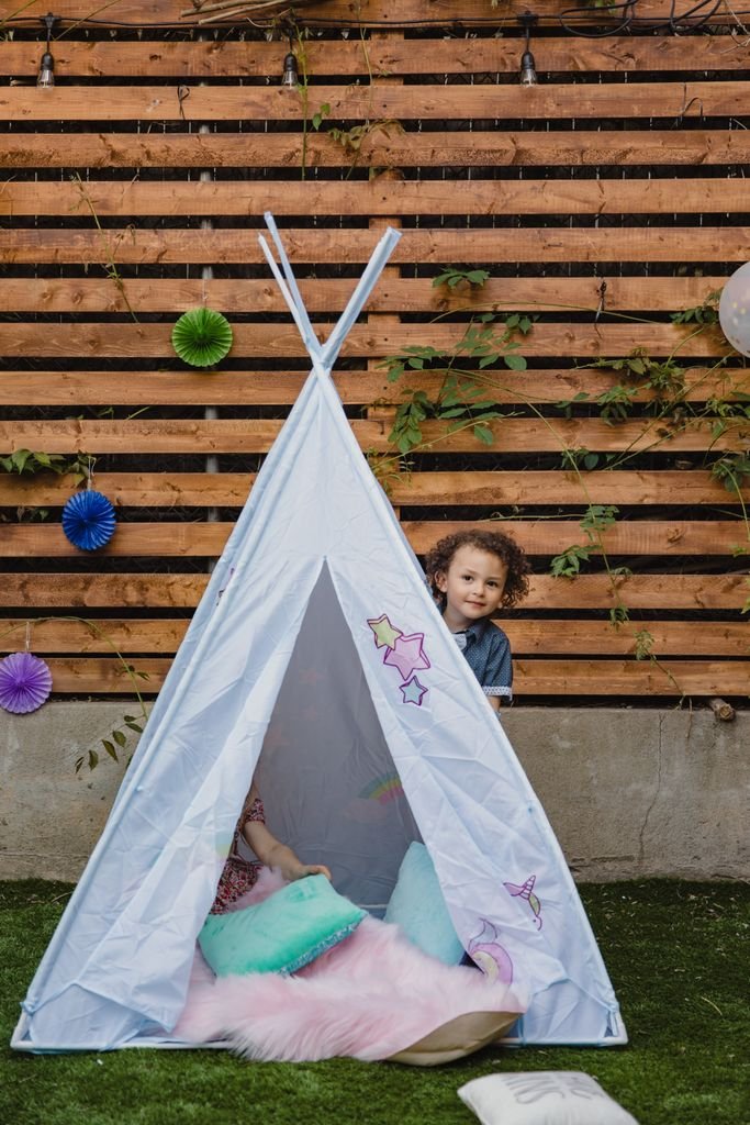 A child plays in a colorful backyard teepee tent with a playful and cozy setting.